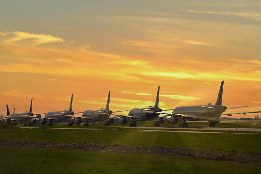 Multiple grounded airplanes parked on the runway just before sunset. Worldwide the airline industry has been taking a hard financially hit due to the Covid - 19, Corona Virus Pandemic.
