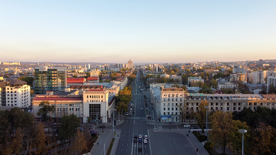 CHISINAU, MOLDOVA - JANUARY 7, 2021: Aerial drone panorama view of downtown at sunset, street with multiple buildings, road with moving cars and yellowed trees