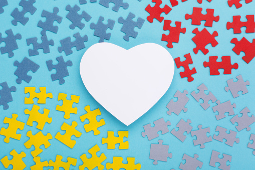 World Autism awareness day background. Creative design for April 2, Autism World Awareness day. Jigsaw colorful puzzle element and white paper heart. Top view, copy space for text.