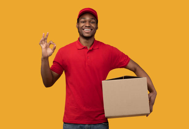 istock Black delivery man holding cardboard box showing okay gesture 1301586809