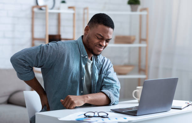 African Guy Having Backache Massaging Aching Back At Workplace Indoor Pain In Back. African American Guy Having Backache Massaging Aching Lower Back Suffering From Pain Sitting At Workplace In Modern Office. Lumbar Ache. Health Problem Concept. backache photos stock pictures, royalty-free photos & images