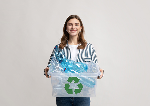 Plastic Recycle. Positive Millennial Woman Holding Container With Bottles For Recycling, Smiling Young Eco-Friendly Lady Agitating For Zero Waste Living And Garbage Sorting Over Grey Background