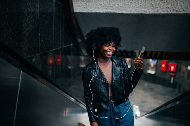 istock Afro woman with earphones using her cellphone while on escalator 1301588598
