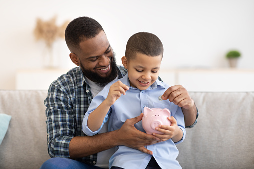 Padre e hijo africanos poniendo dinero en Piggybank en casa photo