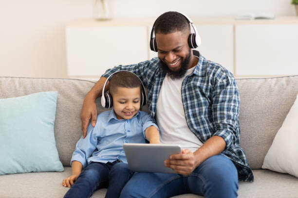 istock African Dad And Son Using Tablet Wearing Earphones Sitting Indoors 1301590720