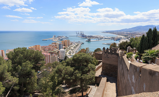 Málaga, Andalusia, Costa del Sol, Spain, April 22nd 2014, sunny cityscape of the seaport of Málaga in the Alboran Sea, with 4 cruise ships and lots of smaller docked boots and high rise buildings in the foreground, seen from the-Castle-of-Gibralfaro with some tourists walking around to explore the fort -  Málaga is the sixth most populous city in Spain, the port is the oldest continuously-operated port in the country