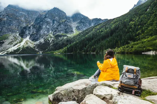 woman backpacker sitting on rock enjoying the view of lake at tatra national park mountains. copy space