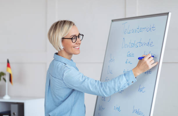 istock Happy young German tutor writing grammar rules on blackboard, giving online lesson from home 1301592122