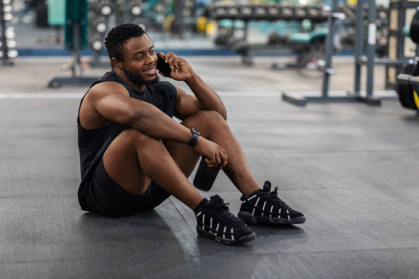 istock Black guy sitting on floor in gym, talking on phone 1301592301
