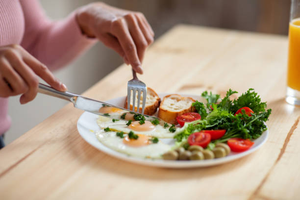 istock Woman eating tasty breakfast in kitchen, using fork and knife, closeup shot 1301592408
