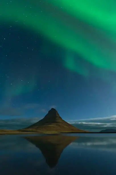 Photo of Northern lights in Iceland. Landscape full of kp5 Aurora Borealis. Amazing nightscape at Kirkjufell, scenic travel destination. Green sky full of stars