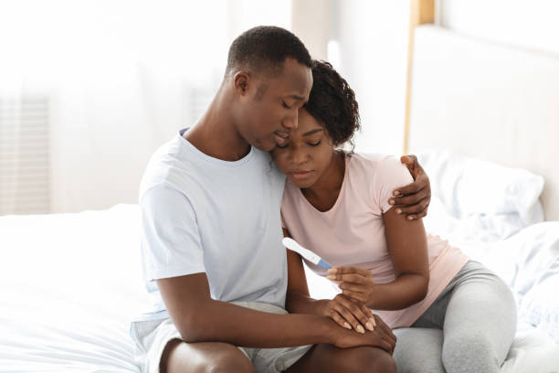 Upset black couple holding negative pregnancy test Upset black couple holding negative pregnancy test, husband hugging his depressed wife, bedroom interior, empty space. Sad african american family looking at pregnancy test, copy space infertility stock pictures, royalty-free photos & images