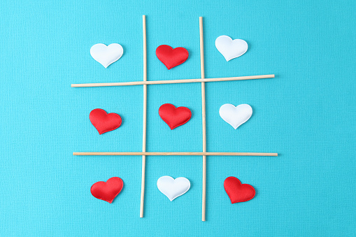 Playing tic tac toe with a white heart and a red heart on a blue background. Concept for love day, Valentine's day, February 14th. Valentine's Day card.