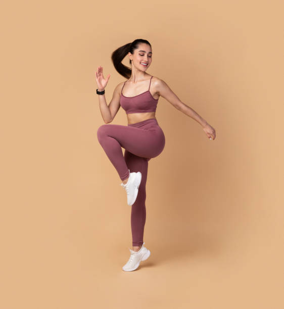 Smiling Young Woman Jumping And Exercising Isolated On Pastel Background Training Concept. Full Length Portrait Of Smiling Fit Young Lady In Sportswear Jumping And Lifting Leg Up, Exercising Isolated On Pastel Background. Studio Shot, Free Space. Energy And Sports sports clothing stock pictures, royalty-free photos & images