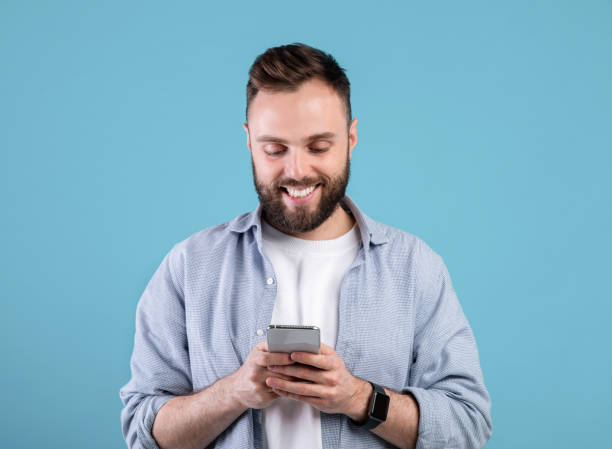 istock Online life soncept. Funky bearded man using cellphone on blue studio background 1301596702