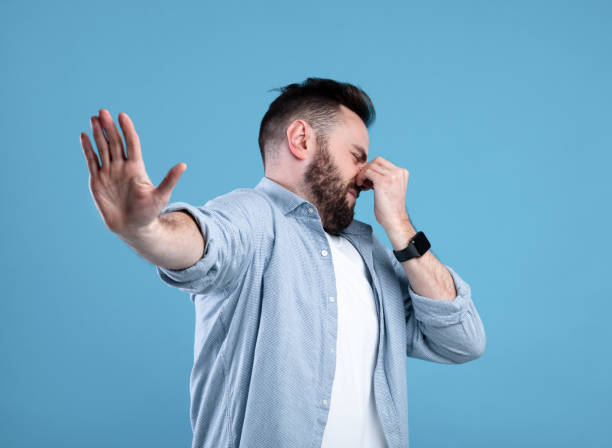 istock Bad smell. Young bearded guy closing his nose and showing STOP gesture, expressing disgust on blue studio background 1301596752