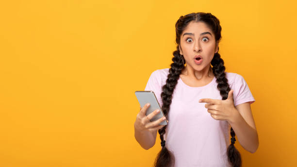 istock Surprised indian woman using mobile phone, pointing at gadget 1301597862
