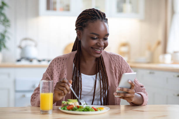 istock Smiling black woman using smartphone while having breakfast in kitchen at home 1301598066