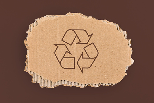 Recycling arrow symbol on piece of cardboard on brown background