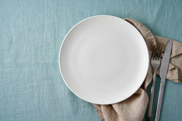 istock Clean empty white plate, fork and knife on pastel blue aquamarine linen tablecloth on table 1301599988