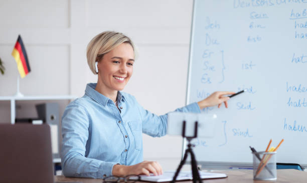 istock Online languages school. Female tutor giving German lesson on internet, using smartphone, explaining grammar to students 1301600119