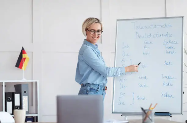 Photo of Studying German online. Friendly female teacher giving foreign language lesson online, explaining grammar to pupils