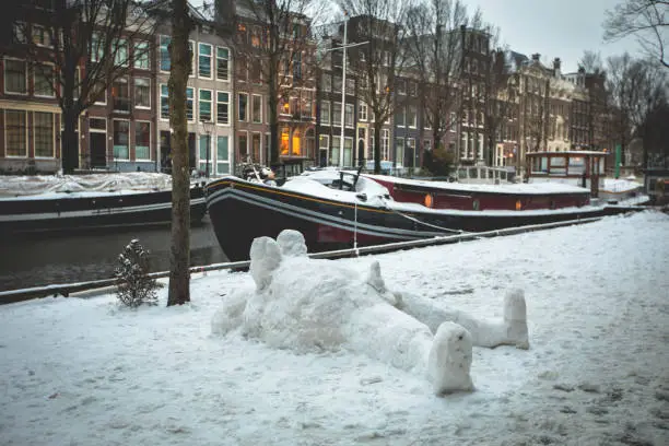 Photo of Winter snow view of Dutch canal and old houses in the historic city of Amsterdam with a lying snow man with a penis, the Netherlands