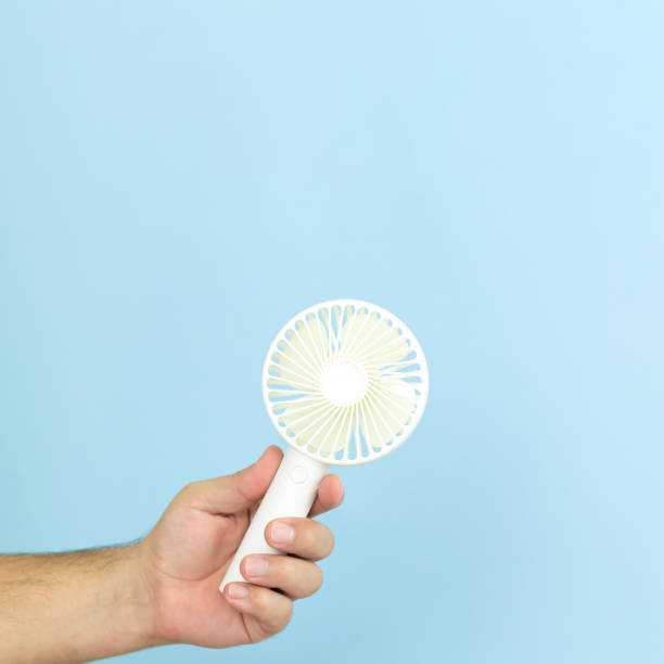 istock Man holding small portable usb fan close-up isolated on blue background 1301601075