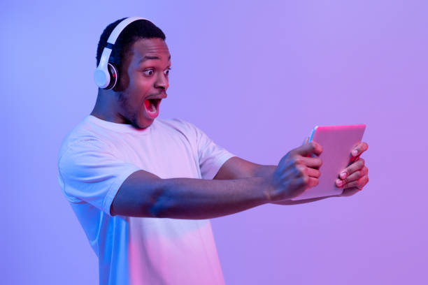istock Surprised black man with digital tablet and wireless headphones playing online games 1301601664