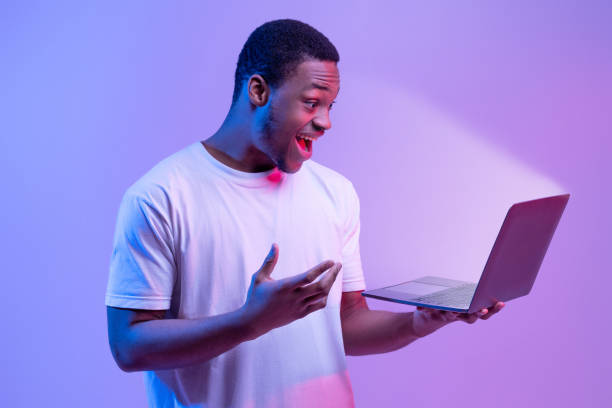 istock Online Offer. Surprised African Man Holding Laptop Looking At Glowing Screen 1301602290