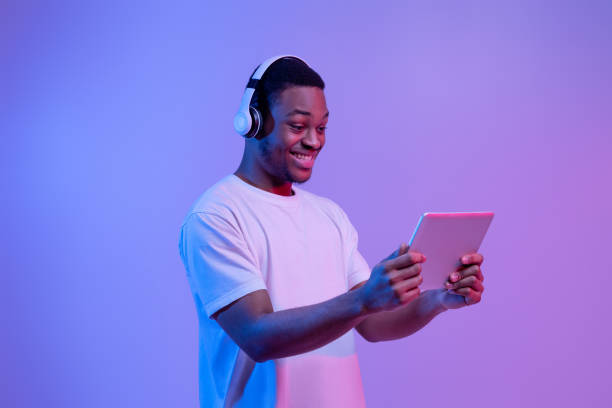 istock Modern Gadgets. Happy Black Man In Headset Using Digital Tablet, Neon Light 1301602352
