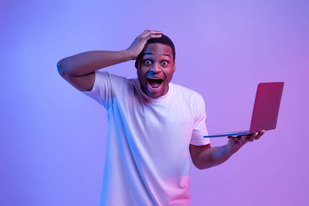 istock Online Win. Shocked black man holding laptop touching head with excitement 1301602381