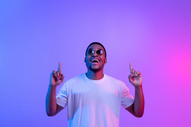 istock Excited Black Guy Standing Under Neon Light Pointing Fingers Up Above Head 1301603081