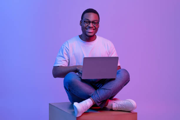 istock Happy Black Student Guy In Eyeglasses Sitting With Laptop In Neon Lighting 1301603173