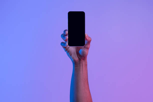 istock Social network and modern technology. Female hand holds phone with blank screen on neon background, close up, copy space 1301603195