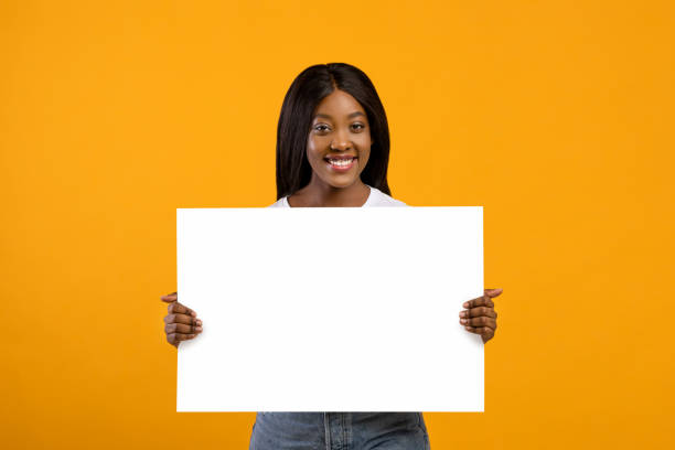 istock Smiling black woman holding blank board for advertisement 1301604110