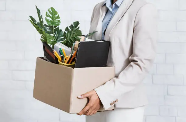 Photo of Unrecognizable black woman holding box of personal belongings, leaving office after losing her job, closeup of hands