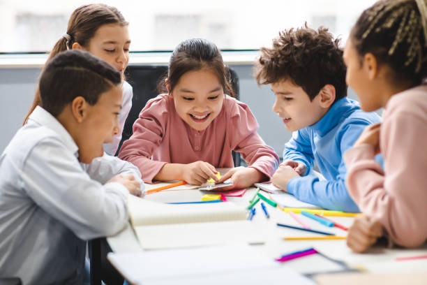 Diverse small schoolchildren using mobile phone at classroom Technology And Pupils Concept. Group of excited multicultural happy junior children sitting at table and using smartphone, playing online mobile games. Modern Device, Gadget Addiction primary school student stock pictures, royalty-free photos & images