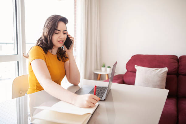 istock Female college student studying and working from home during Covid-19. Using smat phone and laptop.  New normal concept. 1301606370