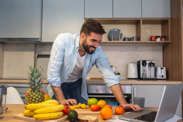 istock Handsome man cooking on kitchen and looking recipe on laptop on table 1301607985