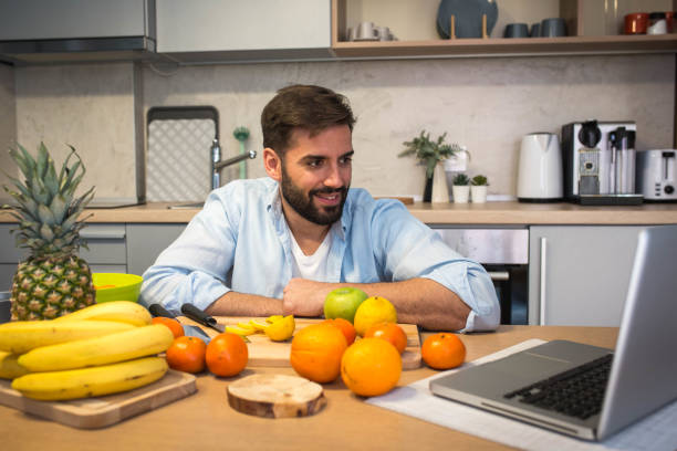 Handsome man cooking on kitchen and looking recipe on laptop on table