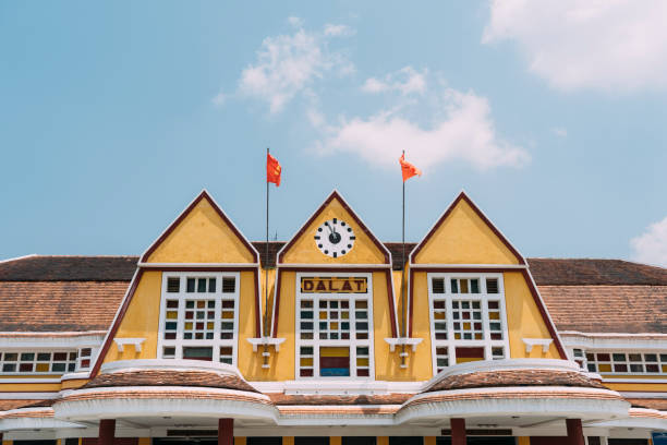 Old train station sign with clock and flags in Dalat, Vietnam. Old yellow train station sign with clock and flags in Dalat, Vietnam. dalat stock pictures, royalty-free photos & images