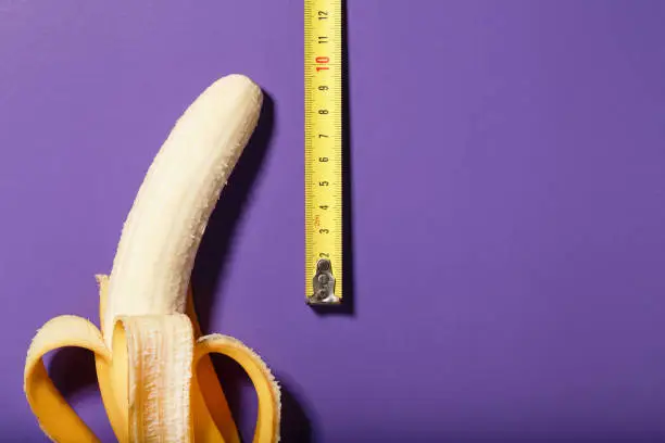 Photo of Yellow banana penis concept measured by measuring tape on a purple background.