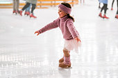 little girl in pink sweater is skating on a winter evening on an outdoor ice rink lit by garlands