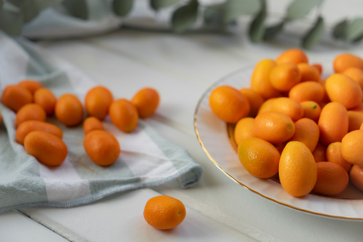 Kumquat fruits into basket on wooden table.