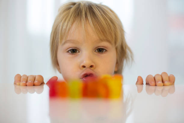 Cute toddler blond boy, looking at colorful gummy bears on the table Cute toddler blond boy, looking at colorful gummy bears, sitting on the table chewy stock pictures, royalty-free photos & images