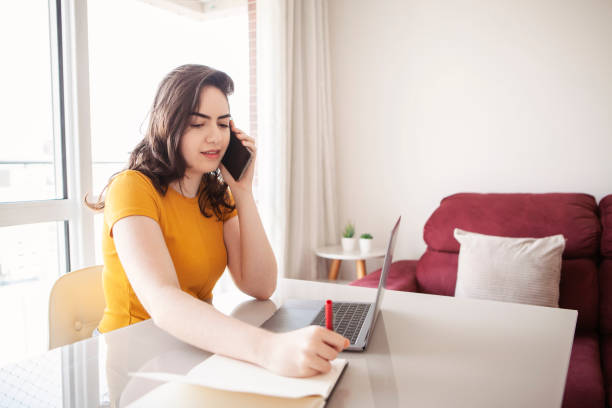 istock Female college student studying and working from home during Covid-19. Using smat phone and laptop.  New normal concept. 1301615383