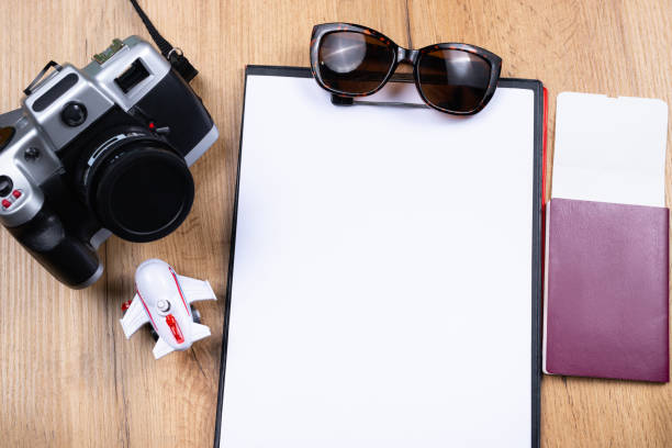 istock Tourism and travel concept. White empty folder sheet, passport with flying ticket, passenger plane figurine, sunglasses and vintage camera on wooden table background. Top view. 1301616856