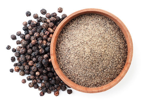 Ground black pepper in a wooden bowl and peppercorns close-up on a white background, isolated. Top view