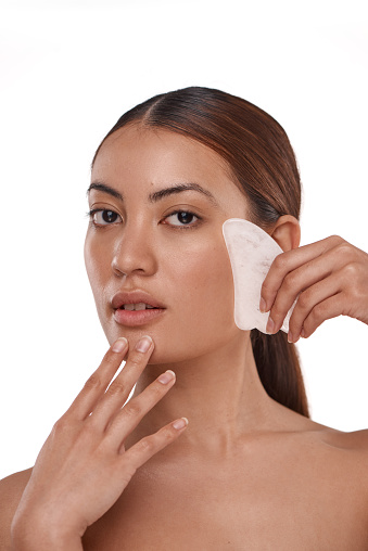Shot of a beautiful woman using a Gua Sha tool on her face